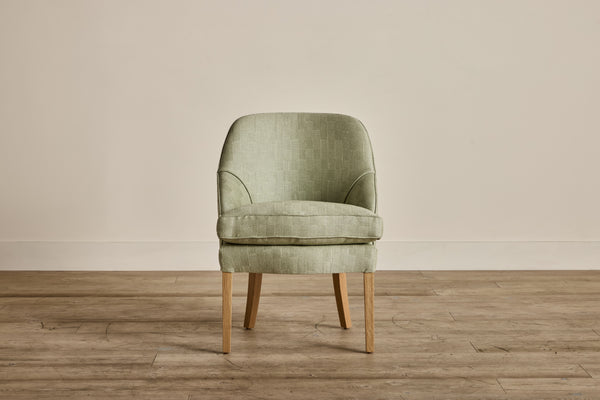 Single upholstered armchair with light green fabric and wooden legs, vintage style, with a rounded backrest and seat cushion.