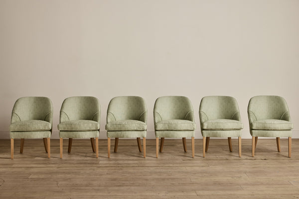 Single vintage armchair with floral patterned fabric in beige, red, blue, and green, with wooden legs, placed against a wall.