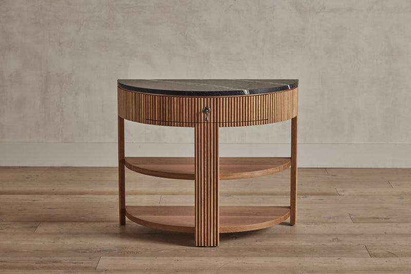 A semi-circular wooden side table with a black marble top, vertical grooved detailing, and a small lock on the front.