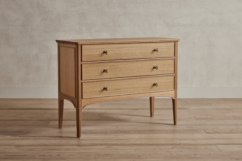 Gray-finished dresser with four drawers and gold knobs, standing on tapered legs.